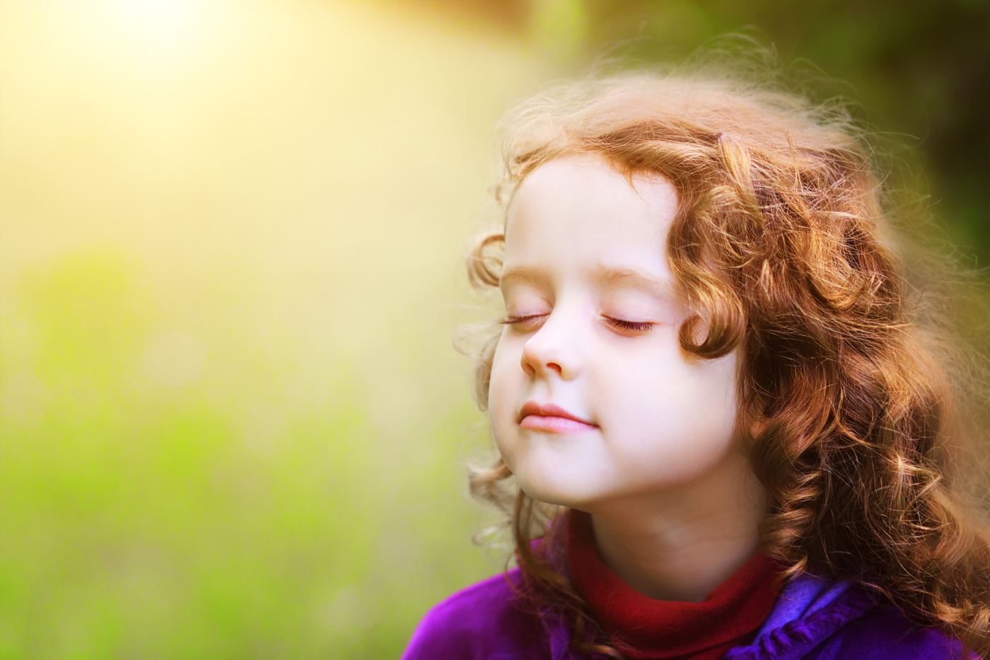A young girl with curly hair resting calmly in the sunshine, eyes closed